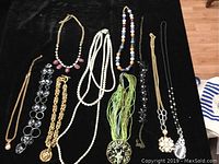 Full view of all 10 necklaces laid out on a dark surface showing variety in styles and colors