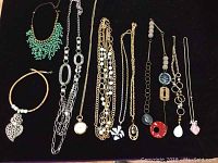 10 assorted costume jewelry necklaces laid out on black surface showing various styles including beaded, chain, and pendant styles