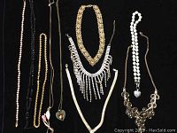 Lot of 10 necklaces laid out including gold-tone chains, white beaded necklaces, rhinestone fringe, and pendants shaped like hearts and teardrops.