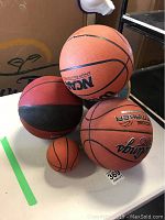 Five basketballs arranged on a white table, four adult basketballs and one small mini basketball.