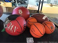 Set of three mini basketballs and small basketball with 8 lb red and black medicine ball and Rawlings football on table
