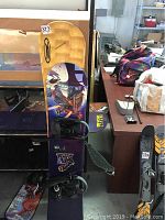 Odyssey 135 snowboard standing vertically showing its purple and yellow top with bindings attached, displaying wear.