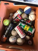 Large orange bin filled with multiple used sports balls including baseballs, softballs, tennis balls, cans of balls, and a blue and white ball.