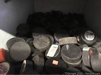 Photo of many used black hockey pucks piled in a box, some with visible logos and stickers.