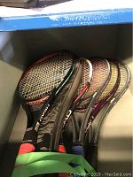 Six tennis rackets with various colorful grips stored vertically, showing general wear.