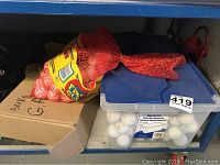 Large red mesh bag of golf balls, a cardboard box labeled bulk golf balls, and a plastic bin containing golf balls.