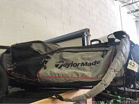 Side view of gray TaylorMade golf bag lying horizontally, showing zippers and brand logo