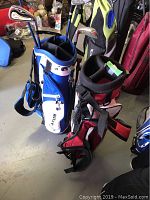 Photo showing two youth golf bags side by side. The blue and white bag contains 5 clubs, the red and black bag is empty.