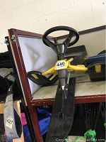 Side angle showing the black steering wheel, yellow frame, black seat and front ski on the snow racer.