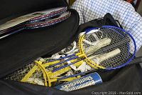 Multiple badminton rackets with yellow and blue frames inside a black carry bag with visible shuttlecocks and a canister of shuttlecocks.