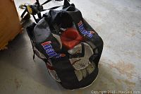 Black mesh Inaria soccer bag filled with soccer balls and cones on concrete floor.