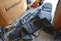 Three sports bags including SIMS branded and unbranded black bags with carrying straps, laid on floor beside large cardboard box.