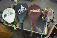Four tennis rackets with three covers laid on surface showing brands and wear.