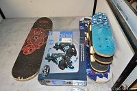 Photo showing the Spider-Man skateboard, a box of Pacific Outdoors rollerblades, and four skateboards of varying sizes with wear.