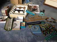 Wide view of assorted trays and loose necklaces scattered on carpet