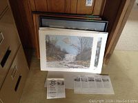 Several prints stacked together showing framed and unframed pieces, with some documentation visible on the floor