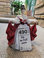 Front view of Royal Doulton lady figurine holding her red skirt, with label showing lot details.