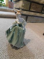 Full view of Royal Doulton porcelain figurine 'Fair Lady' in green dress, showing front and side angles with detailed bonnet and folds in skirt.