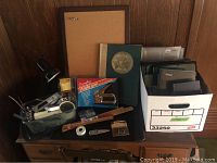 Photo showing assortment of binders, notebooks, cork board, desk lamp, ruler and staple gun on wooden dresser