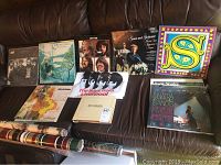 Eight records laid out on sofa: six LPs and two small-sleeve singles (one bootleg sleeve visible).