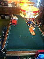 Photo showing full length of green felt Gendron pool table with wood outer frame and corner pockets, with various accessories on table surface including paddles and small bags.