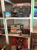 Shelf with boxed steel air pump on top, plastic drawer organizer with screws and small parts, hand screwdrivers in box, extension cords coiled below.