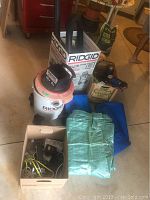 Overview of the lot showing Ridgid wet/dry vac, folded tarps, box with miscellaneous items, and other items.