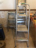 Three aluminum step ladders positioned together against a brick and pegboard wall, showing overall condition and size difference.
