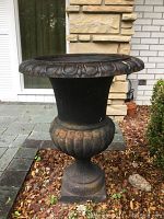 Front view of cast iron garden urn showing decorative rim and bulbous base with rust spots and patina.