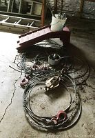 Photo showing red metal car ramp, coiled steel cables with metal hooks, metal pulley on floor.