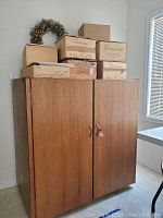 Closed view of the wooden wine refrigerator cabinet with stacked wooden wine boxes and dried flower wreath on top.