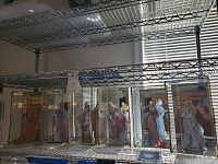 Six figurines displayed side by side in glass cases on metal shelving