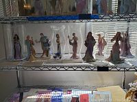 Shelf view of nine porcelain princess figurines each in clear plastic display cylinder