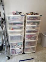 Two plastic wheeled storage drawer units filled with various craft supplies including ribbons, wire cutters, and other materials.