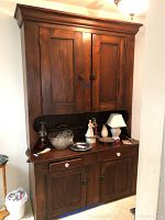 Full view of vintage wooden hutch with upper cabinet doors, open shelf with items, two drawers with white knobs below, and double door lower cabinet.