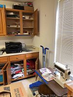 Overview of the sewing area showing an open cabinet with sewing supplies, sewing table with a sewing machine, swivel stool, and exercise stepper nearby.