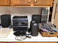 Full view of Sony audio equipment on countertop including boombox, two sets of speakers, portable Discman player with charger, baskets with CDs, and vertical CD storage racks.