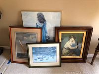 Four framed pieces leaning against wall showing varied artwork including sailboat, woman in blue shawl, sheep, and mother with child.
