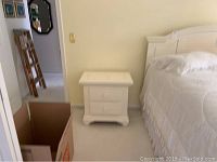 Two white nightstands in a bedroom setting, placed against a light-colored wall, one next to a bed with white bedding.