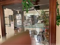 Glass cabinet with multiple Asian collectibles including ceramic plates, porcelain and brass vases, and translucent figurines.