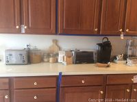 Kitchen countertop with silver Waring 4-slice toaster, silver Delonghi toaster oven, black Keurig coffee maker, and Cuisinart food processor base.