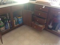 Kitchen cabinets and drawers open showing cleaning products and kitchen supplies