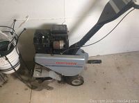 Side view of the Craftsman tiller on floor showing branding, wheel, and tiller blades.