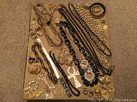 Overhead photo showing multiple pieces of black and gold costume jewelry laid on a beige surface including necklaces, earrings, rings, bracelets, and brooches.
