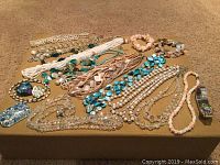 Overview of costume jewelry lot on brown surface including multiple necklaces with beads, pendants, faux pearls, and bracelets.