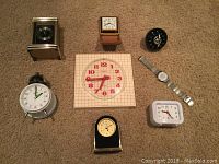 Overhead photo of all eight time pieces showing various styles and sizes on carpet