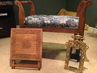 Wooden hall bench with curved carved arms and floral upholstery, small ornate gold-colored mirror, and foldable wooden stand with carved floral border and inlay, on carpeted floor.
