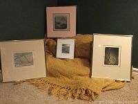 Four framed art prints laid out against a mustard colored woven blanket with various mat and frame styles.