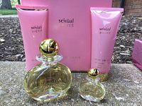 Full lot including large and small perfume bottles with gold spherical caps, two pink tubes of body lotion, and pink box with gold text in the background. All items on outdoor surface.