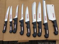 Full view of 9 knives showing different blade shapes including boning, carving, slicing and cleaver styles with black handles and Barclay Lausanne labels.